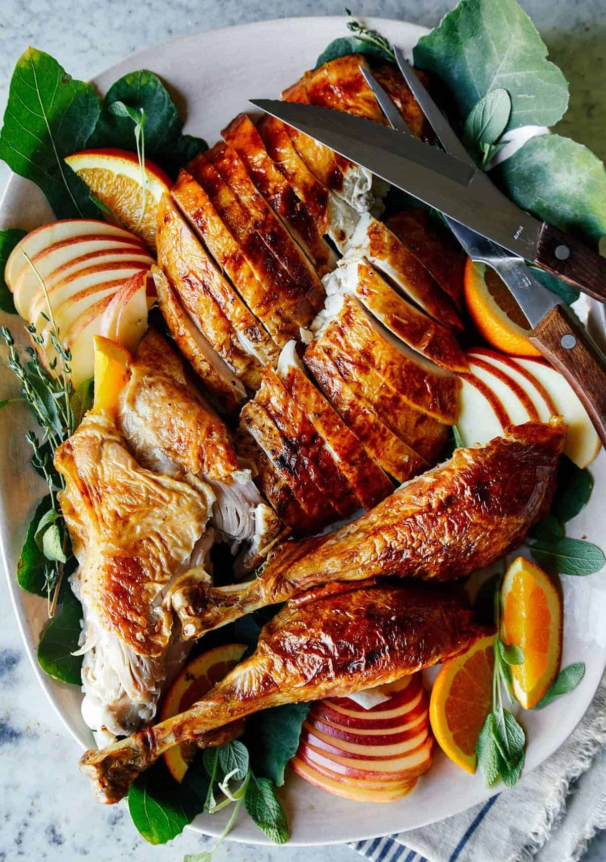 A sliced citrus dry brined turkey on a platter with apple and orange garnish.