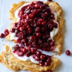 A crostata topped with yogurt filling and cranberries with the end cut off.