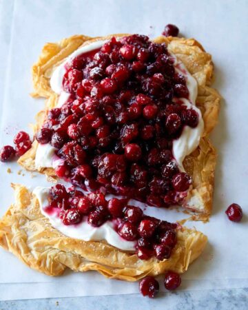 A crostata topped with yogurt filling and cranberries with the end cut off.
