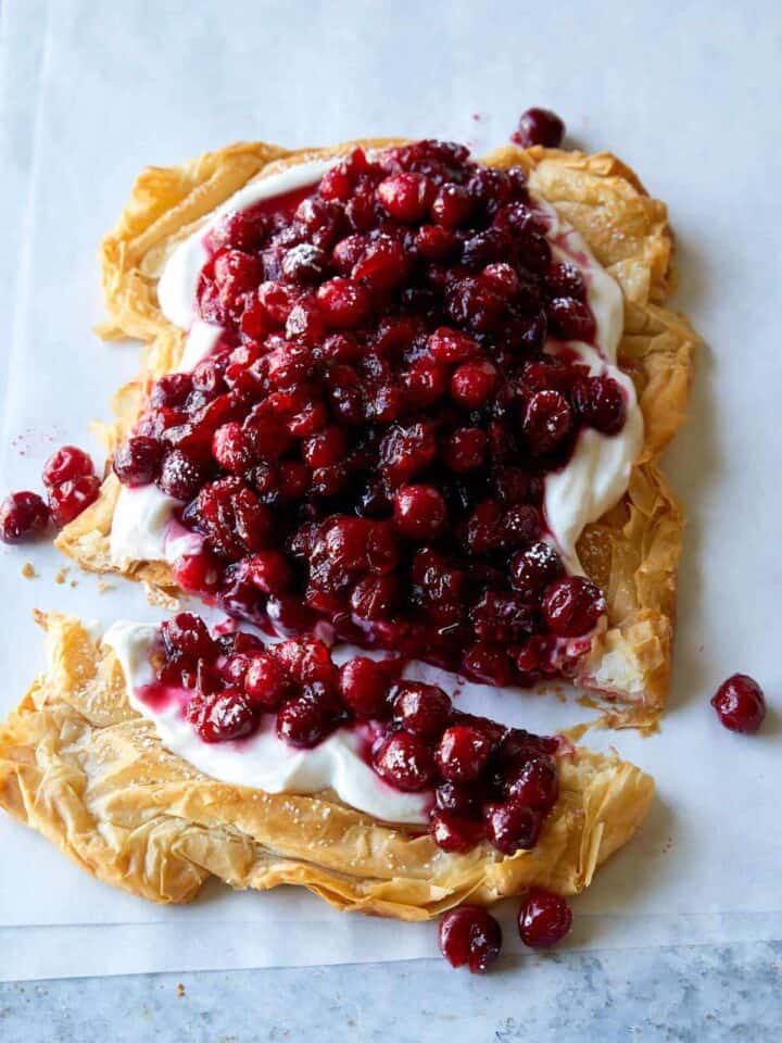 A crostata topped with yogurt filling and cranberries with the end cut off.