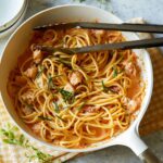 Creamy lobster pasta in a white pot with metal tongs.