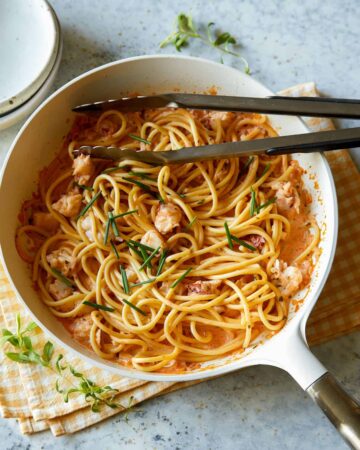 Creamy lobster pasta in a white pot with metal tongs.