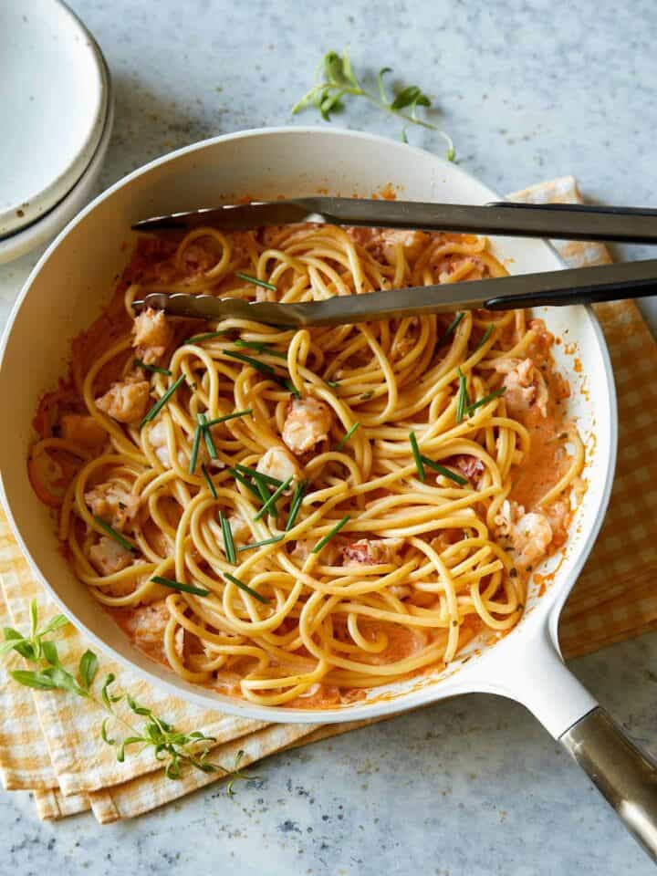 Creamy lobster pasta in a white pot with metal tongs.