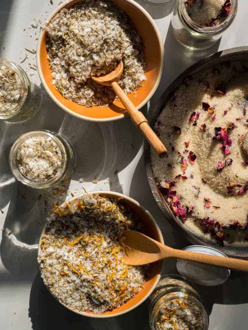 Mixing bowls of a variety of DIY salts and sugars with wooden spoons.