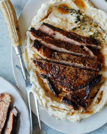 Seared ribeye over brown butter mashed potatoes with a roasting fork.