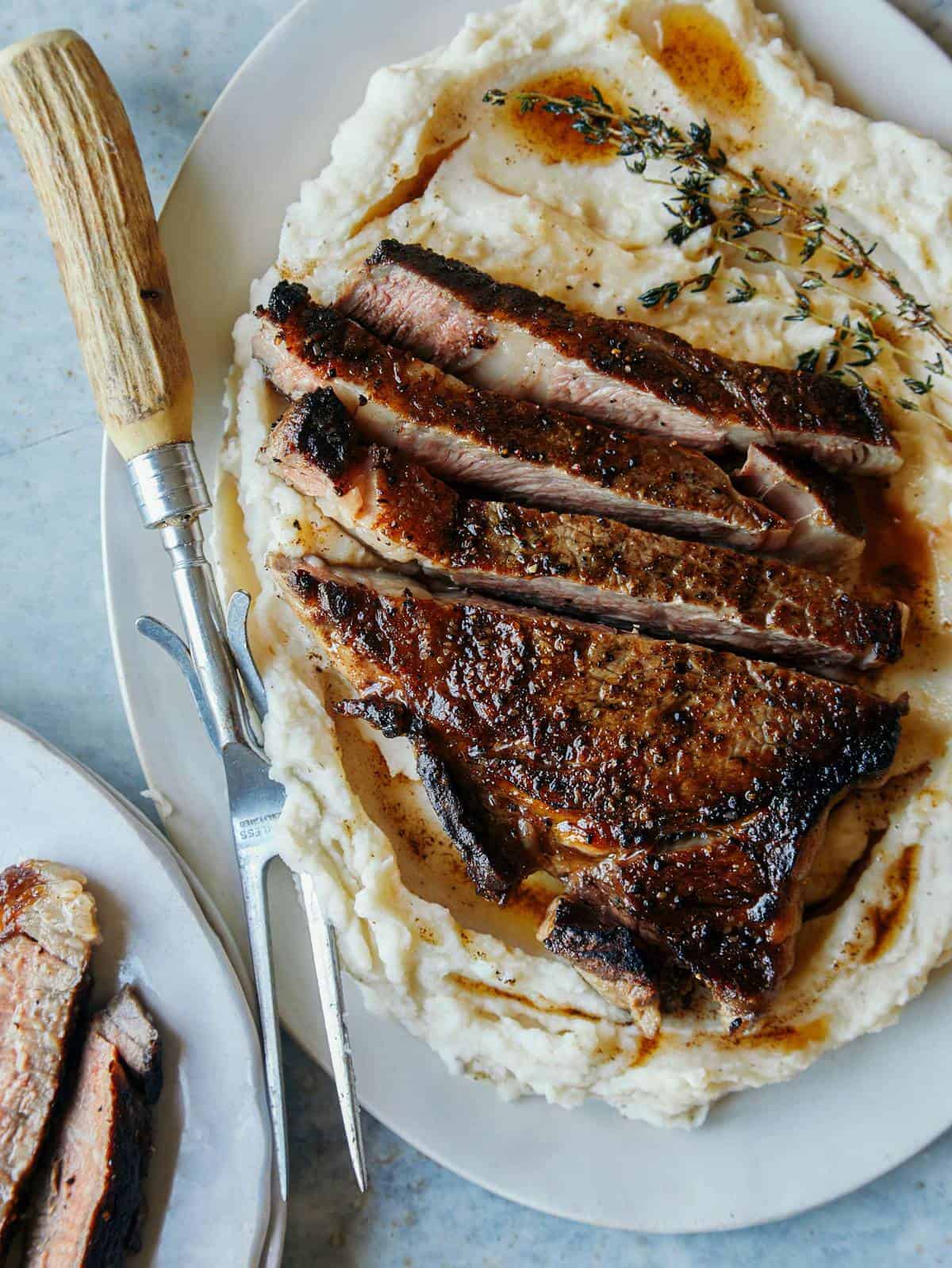 Seared ribeye over brown butter mashed potatoes with a roasting fork.