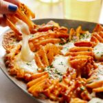 A close up of a hand taking poutine with waffle fries off a plate.