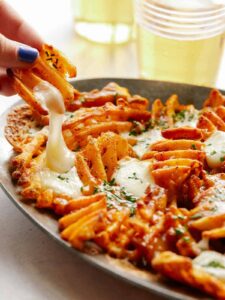 A close up of a hand taking poutine with waffle fries off a plate.