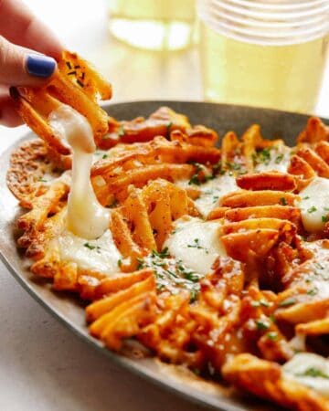 A close up of a hand taking poutine with waffle fries off a plate.