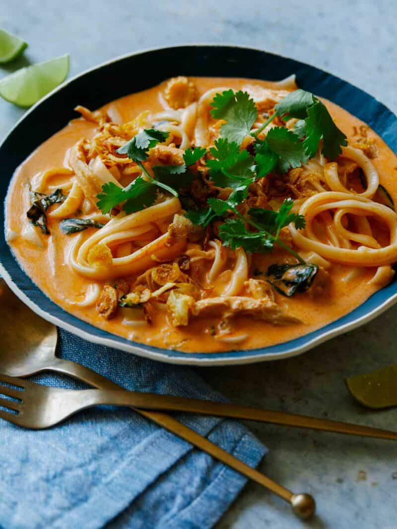 Spicy Thai Red Curry Soup recipe in a bowl topped with cilantro with lime wedges nearby. Ready to be eaten!