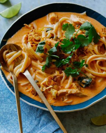 Bowl of spicy thai red curry soup with a spoon and fork.