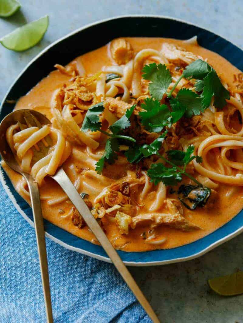 Spicy Thai Red Curry Soup recipe topped with fresh cilantro with lime wedges on the side. A fork is twisted with some noodles. 