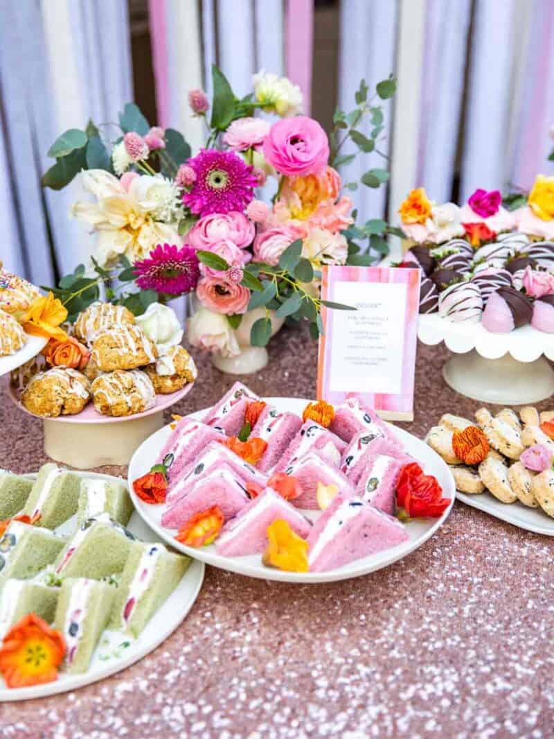 A table full of tea sandwiches and a variety of baked goods with a floral arrangement.