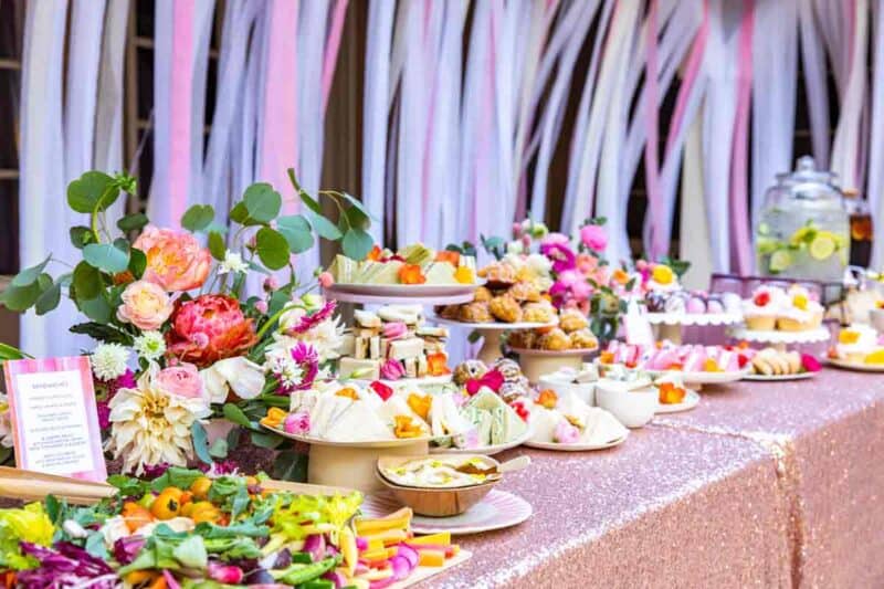 A table full of tea sandwiches and small bites with a floral arrangement.