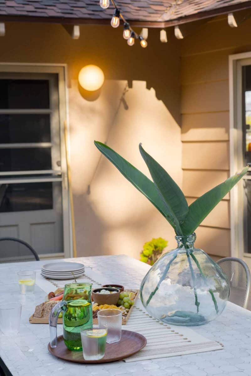 A vase with leaves on a table next to a platter of food.