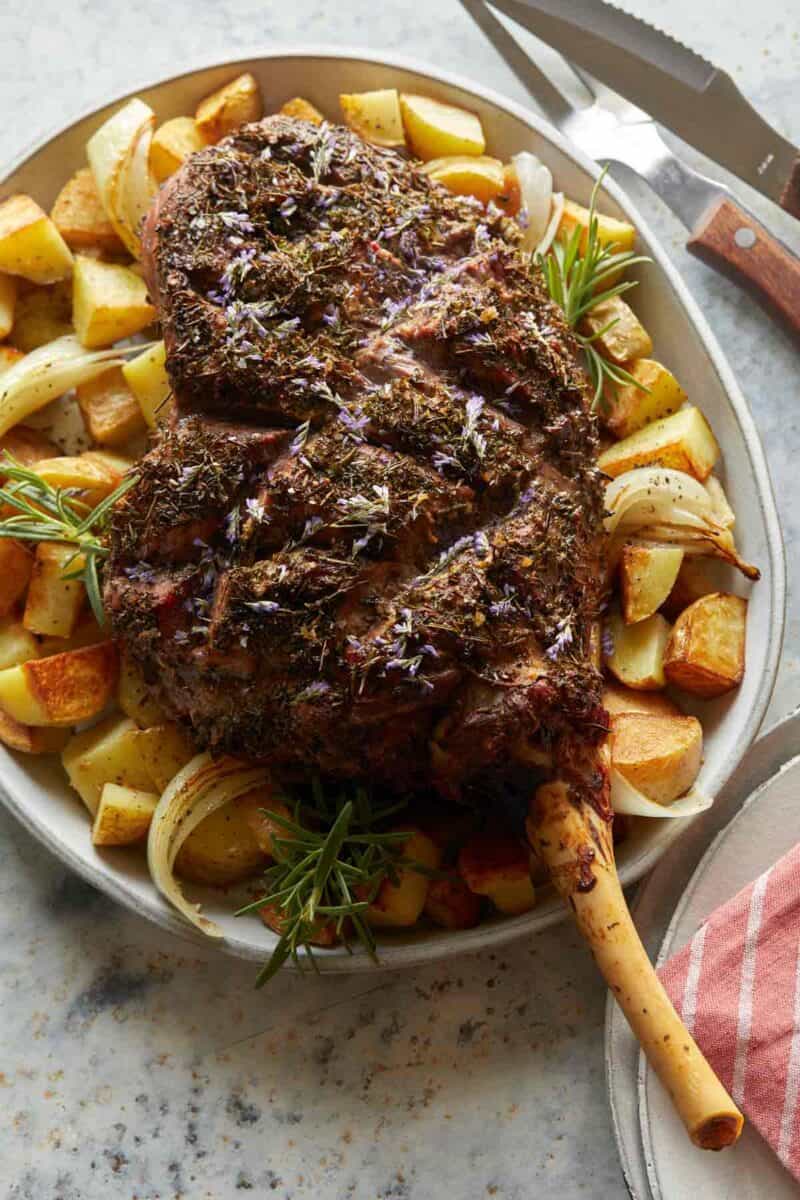 Herb crusted leg of New Zealand grass fed lamb on a plate with potatoes.