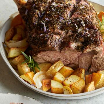 Herb crusted leg of New Zealand grass fed lamb on a plate with potatoes.