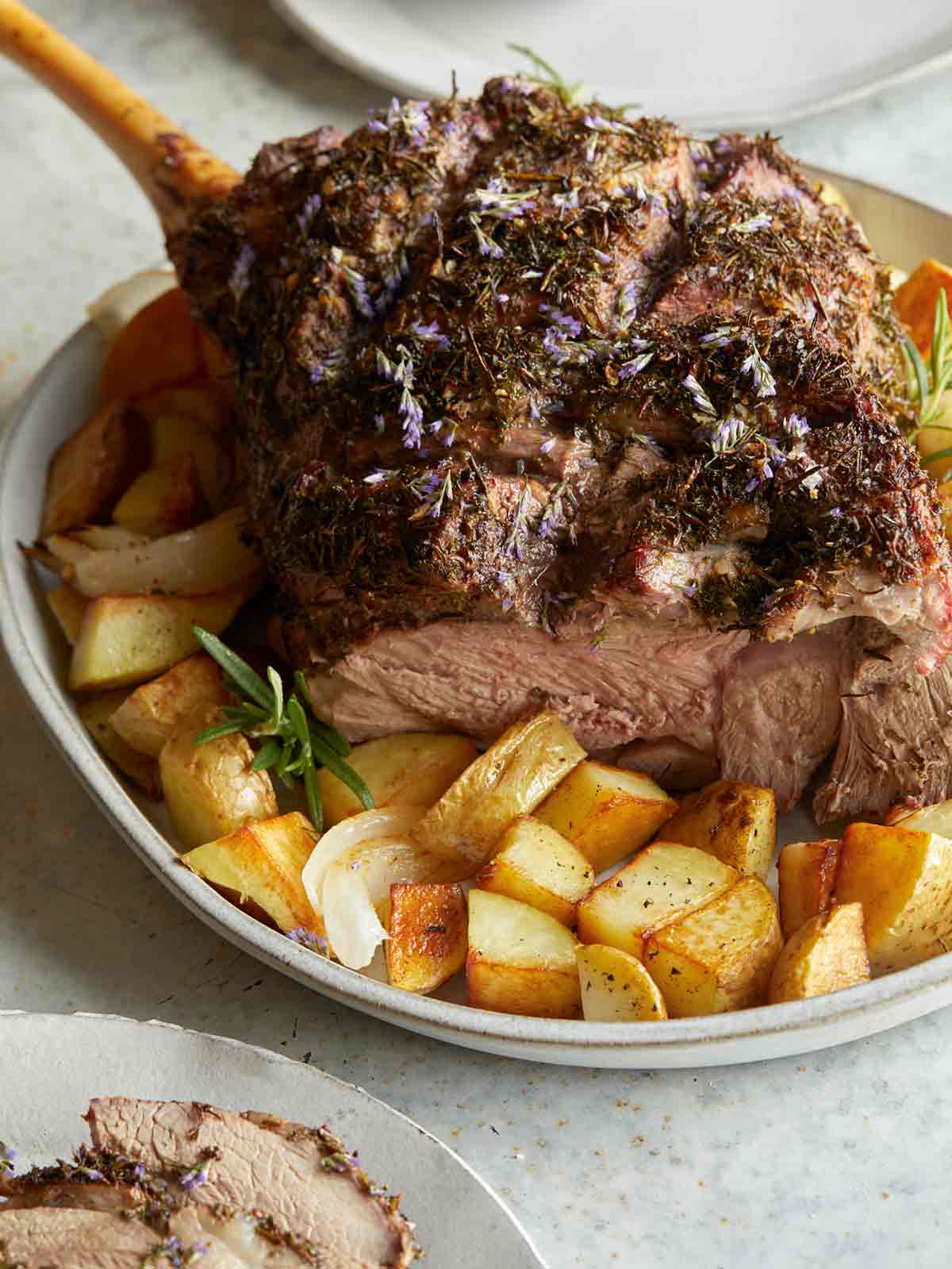 Herb crusted leg of New Zealand grass fed lamb on a plate with potatoes.