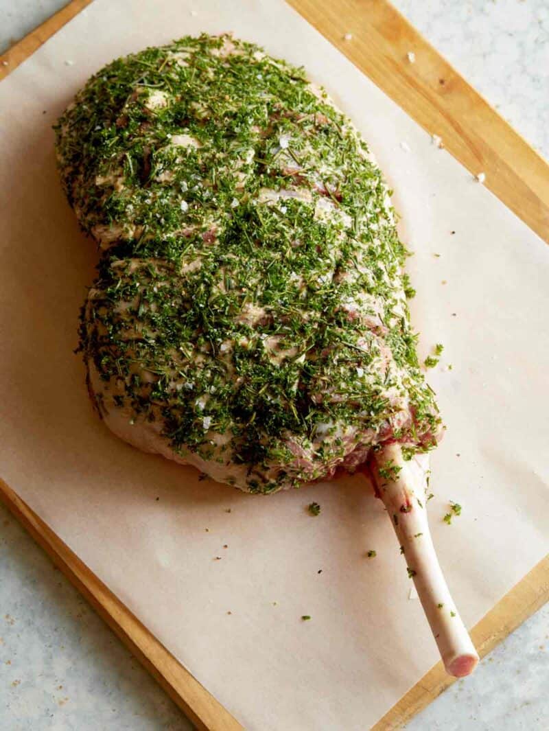 Raw, herbed leg of lamb on a cutting board.