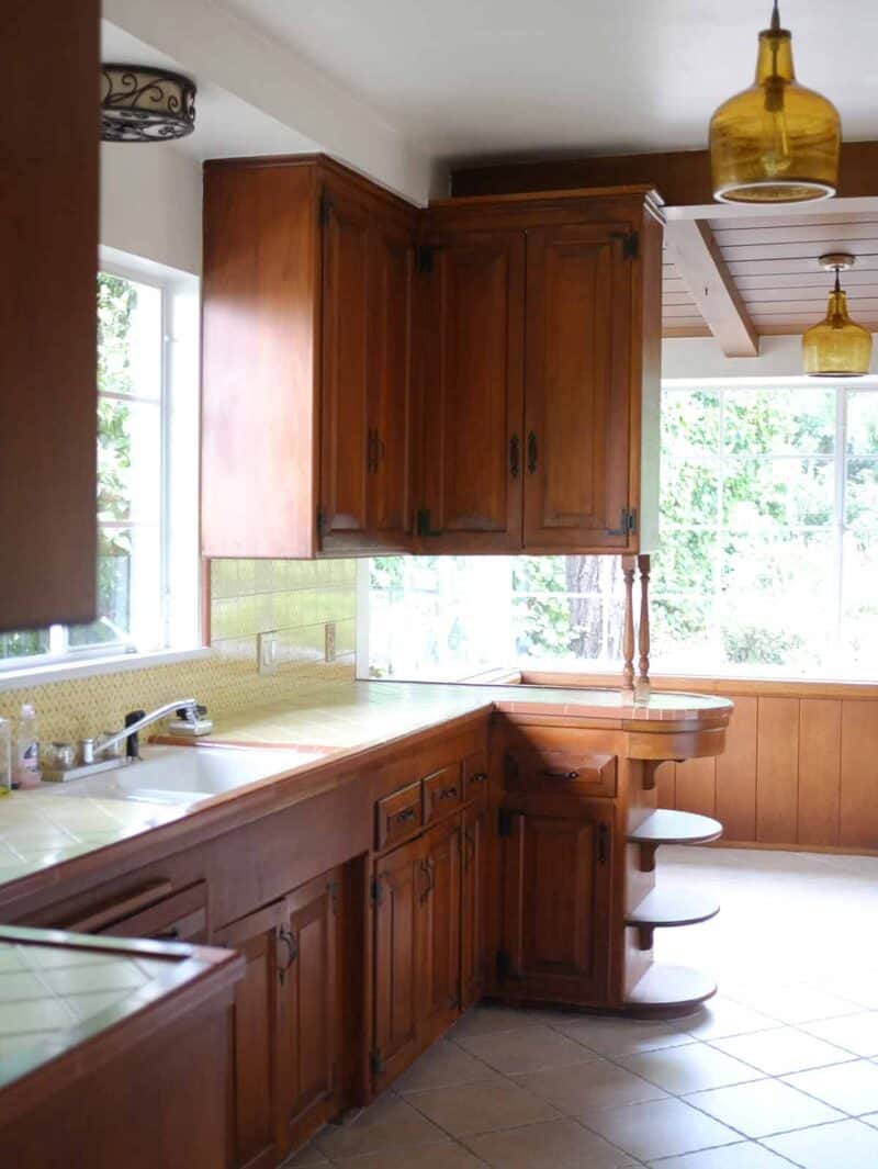 A kitchen sink with wooden cabinets and breakfast nook.