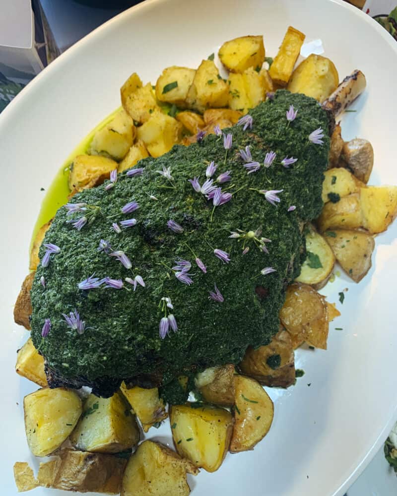 Herb crusted leg of New Zealand grass fed lamb on a plate with potatoes.