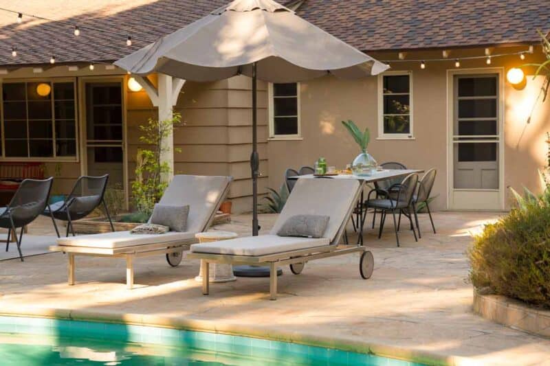 Chaise lounges with umbrella and a dining table by a pool.