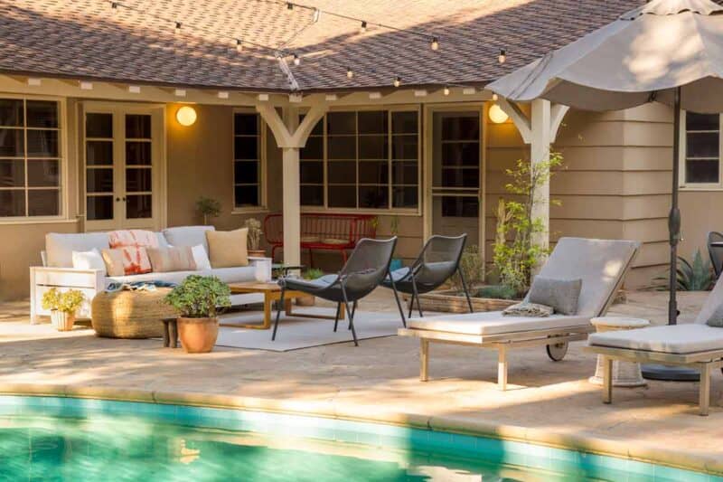 A furnished patio with a couch, chairs, and chaise lounge by a pool.