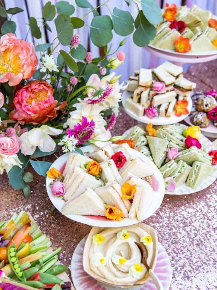 A table full of tea sandwiches and a floral arrangement.