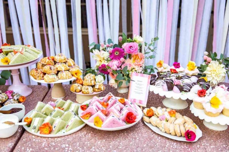 A table full of tea sandwiches and a variety of baked goods with a floral arrangement.