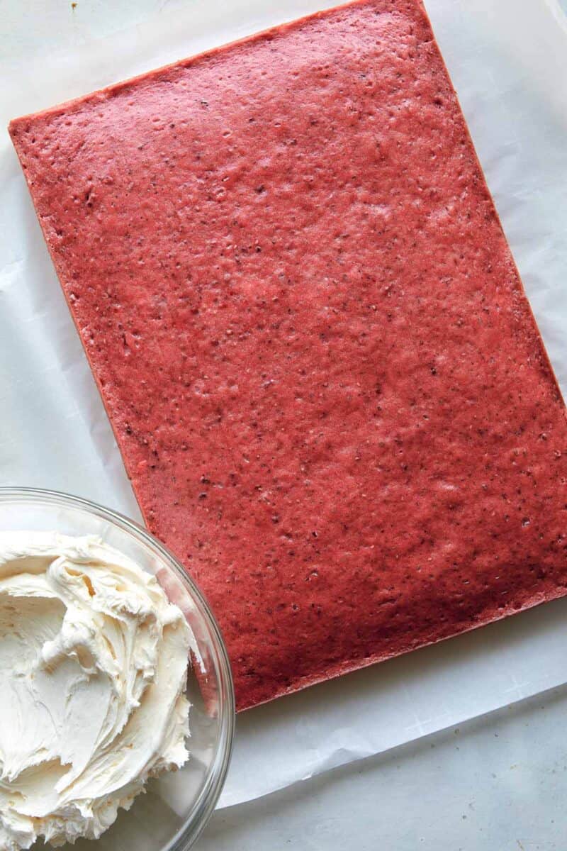 A whole raspberry sheet cake with frosting in a bowl on the side.