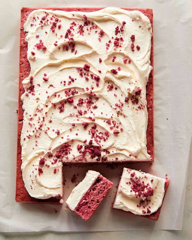 A whole raspberry sheet cake with white chocolate frosting with slices cut off.