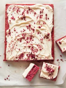 A whole raspberry sheet cake with white chocolate frosting with slices cut off.
