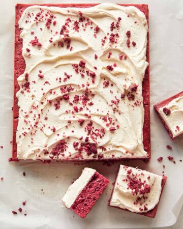 A whole raspberry sheet cake with white chocolate frosting with slices cut off.