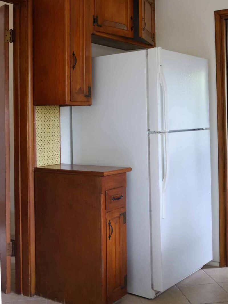 A refrigerator next to wooden cabinets.