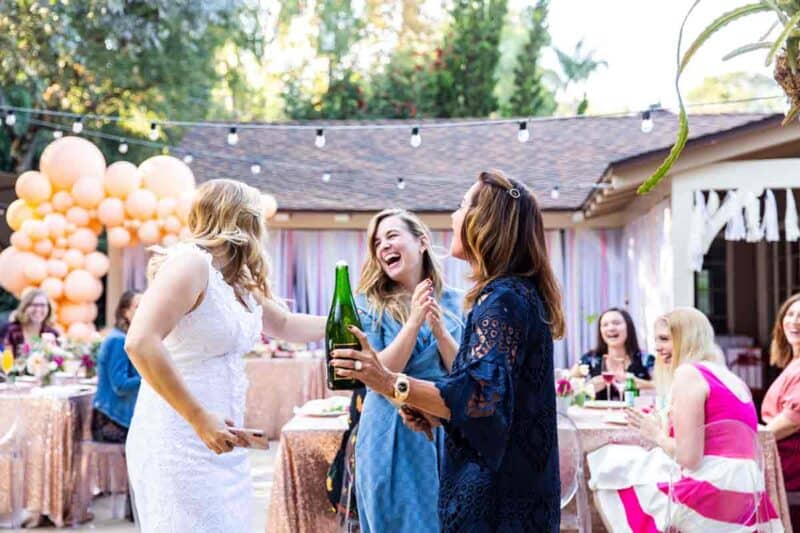 A group of beautiful, smiling women with a sabered champagne bottle in hand.