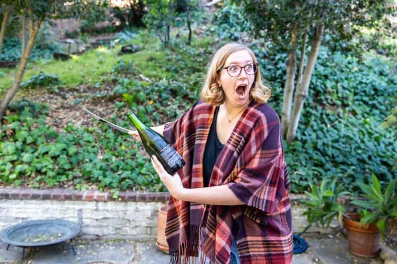 An excited woman using a saber on a champagne bottle in a garden.