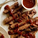 Sliced slow cooker BBQ Wagyu beef brisket with sauce drizzled and on the side.