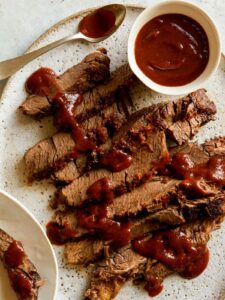 Sliced slow cooker BBQ Wagyu beef brisket with sauce drizzled and on the side.