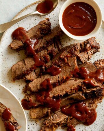 Sliced slow cooker BBQ Wagyu beef brisket with sauce drizzled and on the side.