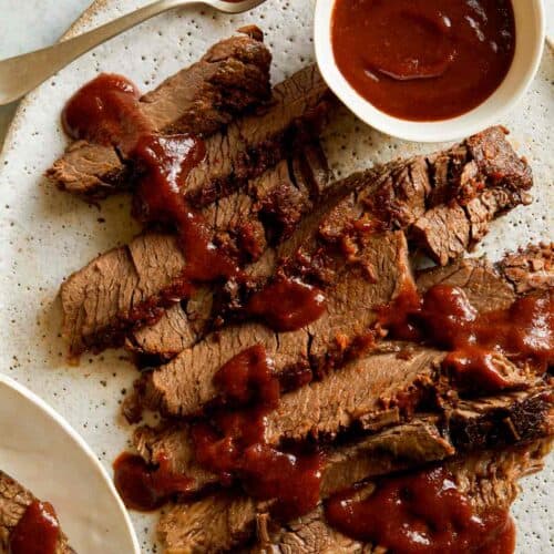 Sliced slow cooker BBQ Wagyu beef brisket with sauce drizzled and on the side.