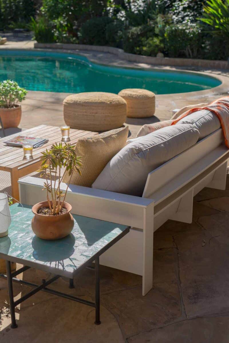 A furnished patio with a couch and table by a pool.