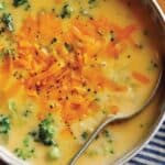 A close up of a bowl of broccoli cheddar soup with a spoon.