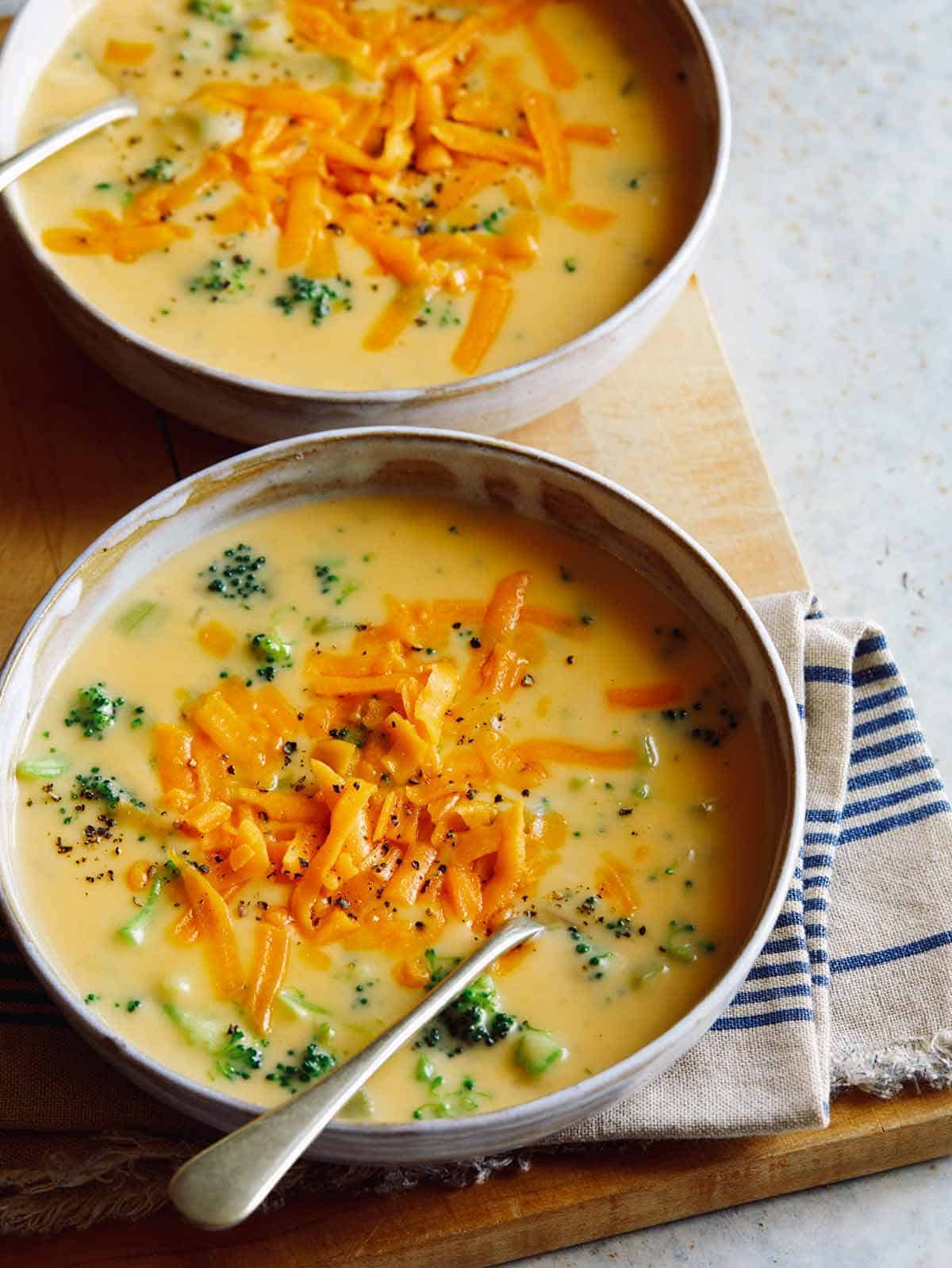 Two bowls of cheddar broccoli soup topped with some more shredded cheese.