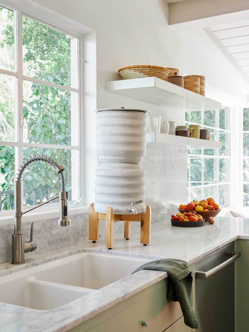 A kitchen sink by a window, Bosch dishwasher below with water filter on the counter.