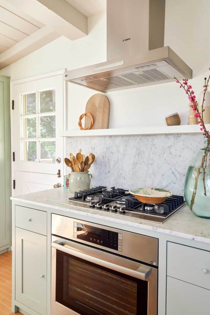 Stove top oven with marble countertops and backsplash with hood vent.