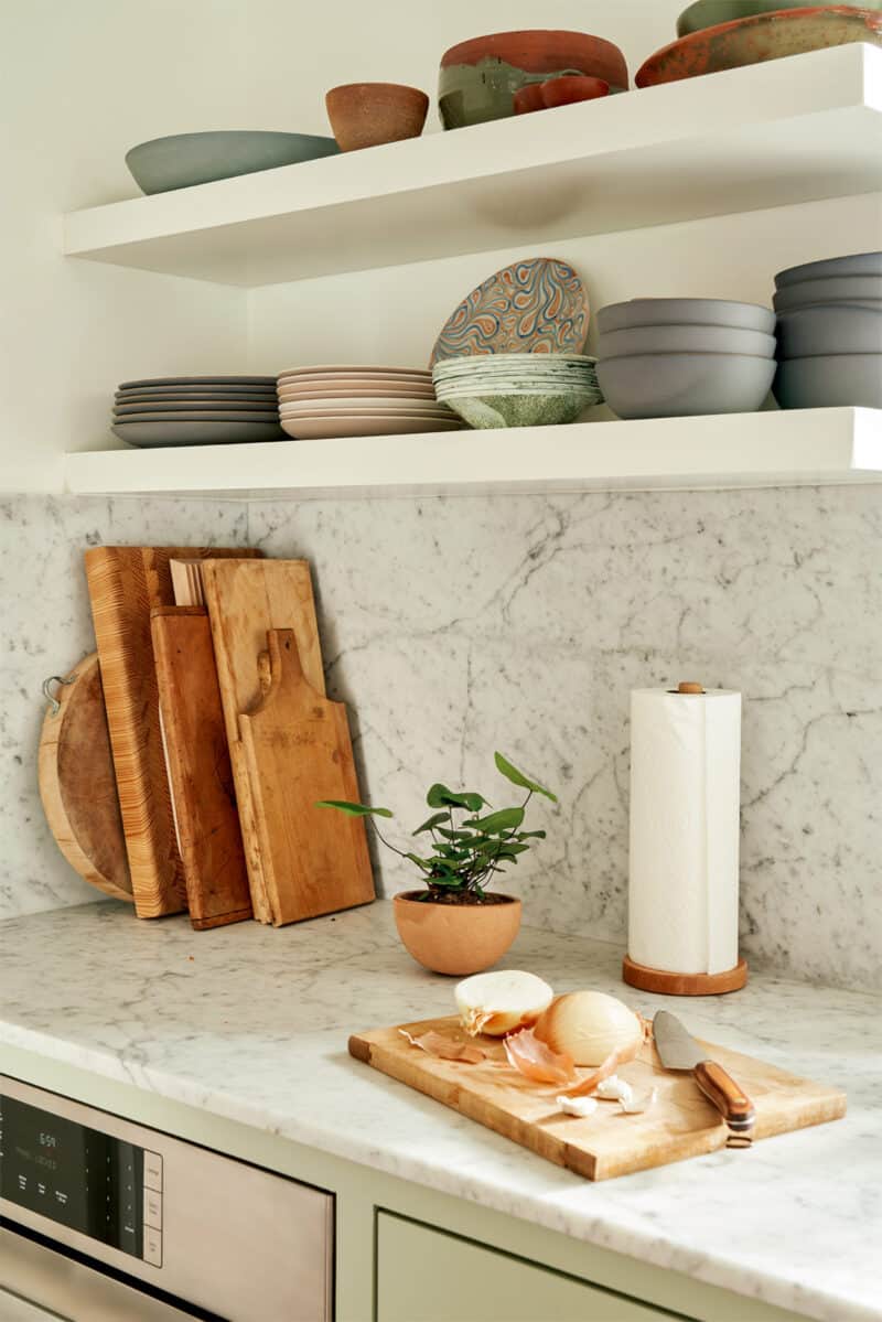 Floating shelves with plates and bowls over a marble backsplash and countertop.