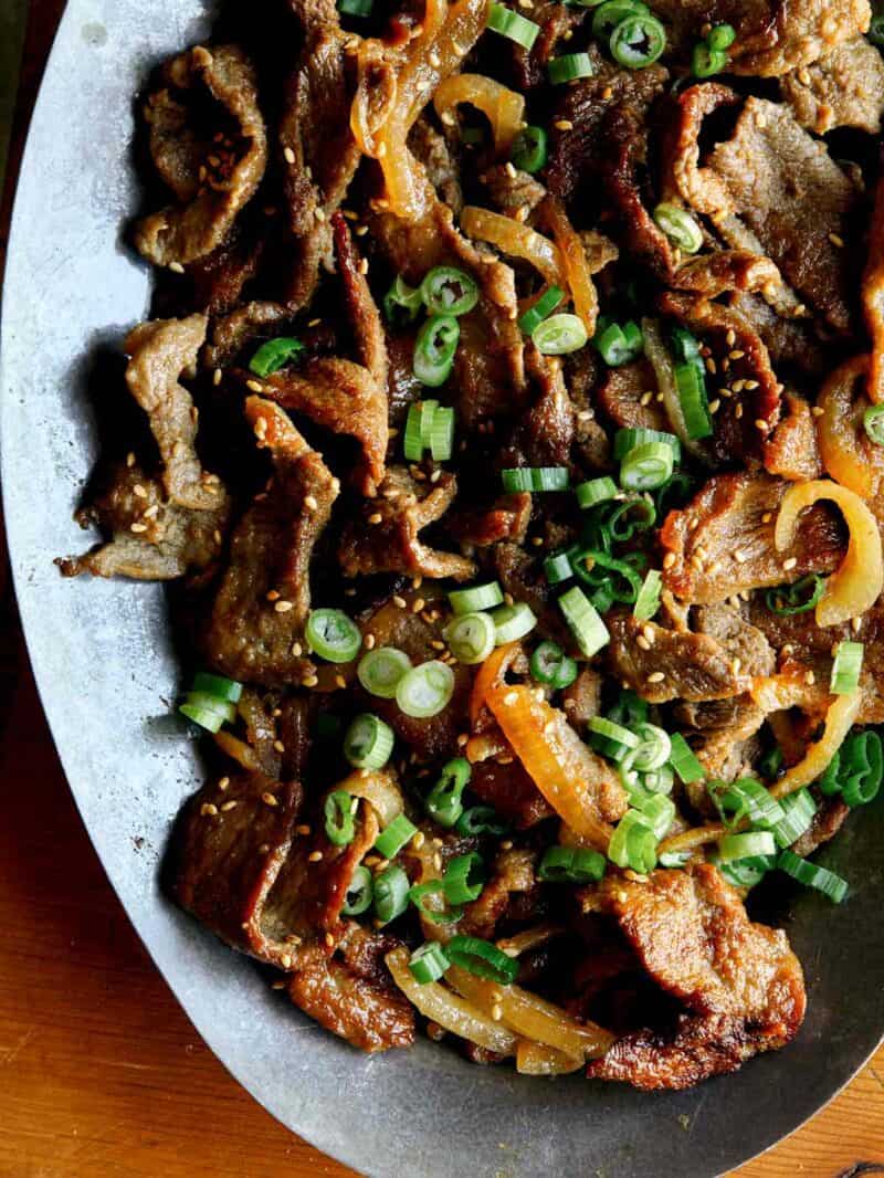 A close up of Korean beef bulgogi with green onions on a plate.
