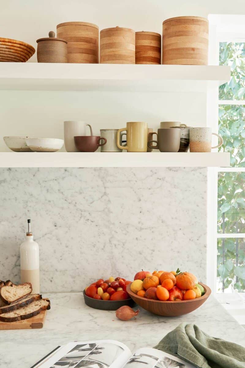 Floating shelves with mugs over a marble backsplash and countertop.