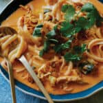 Bowl of spicy thai red curry soup with a spoon and fork.