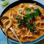 Bowl of spicy thai red curry soup with a spoon and fork.